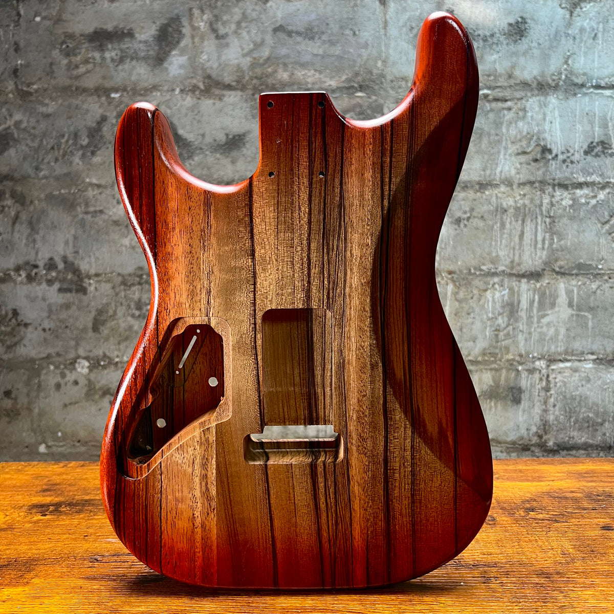 Strat-style guitar body front view with routed cavities and glossy red-brown finish