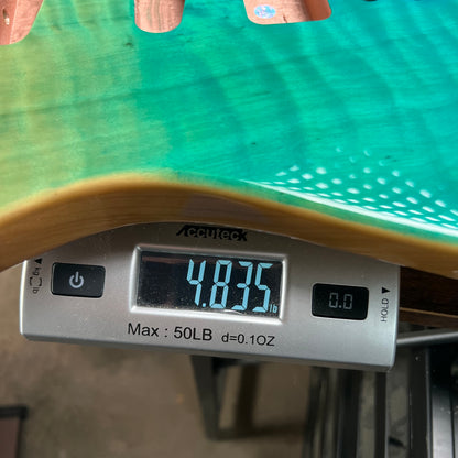 Teal glossy Tele-style guitar body edge with flame maple grain near hardware area