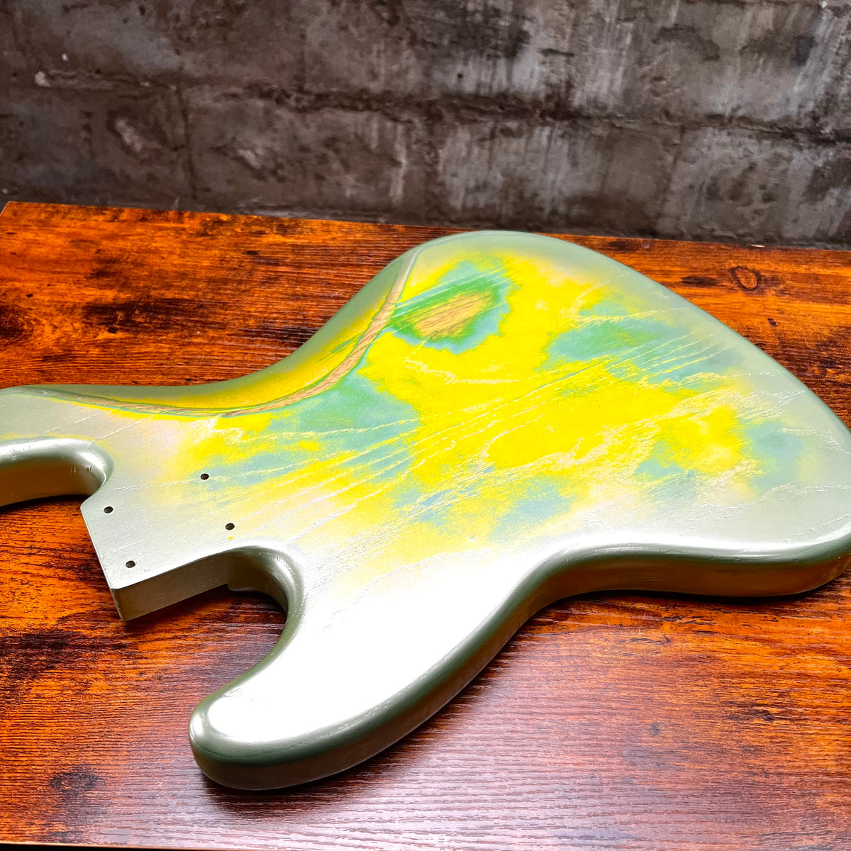 Green and yellow bass body laid on wood, showing contoured edge and holes