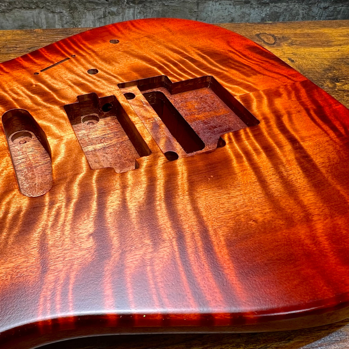 Flamed maple guitar body top view with routed pickup cavities and mounting points