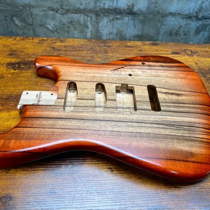 Strat-style guitar body, red-brown finish with bridge and pickup routes visible