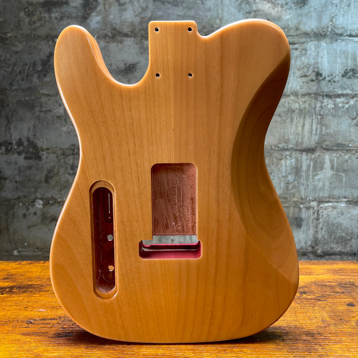 Unfinished light wood guitar body with routed cavities and strap-button holes