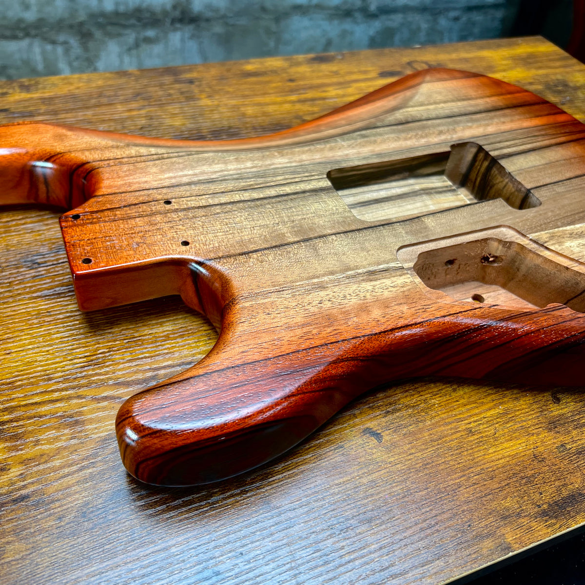 Strat-style guitar body front with pickup cavities and exposed wood grain