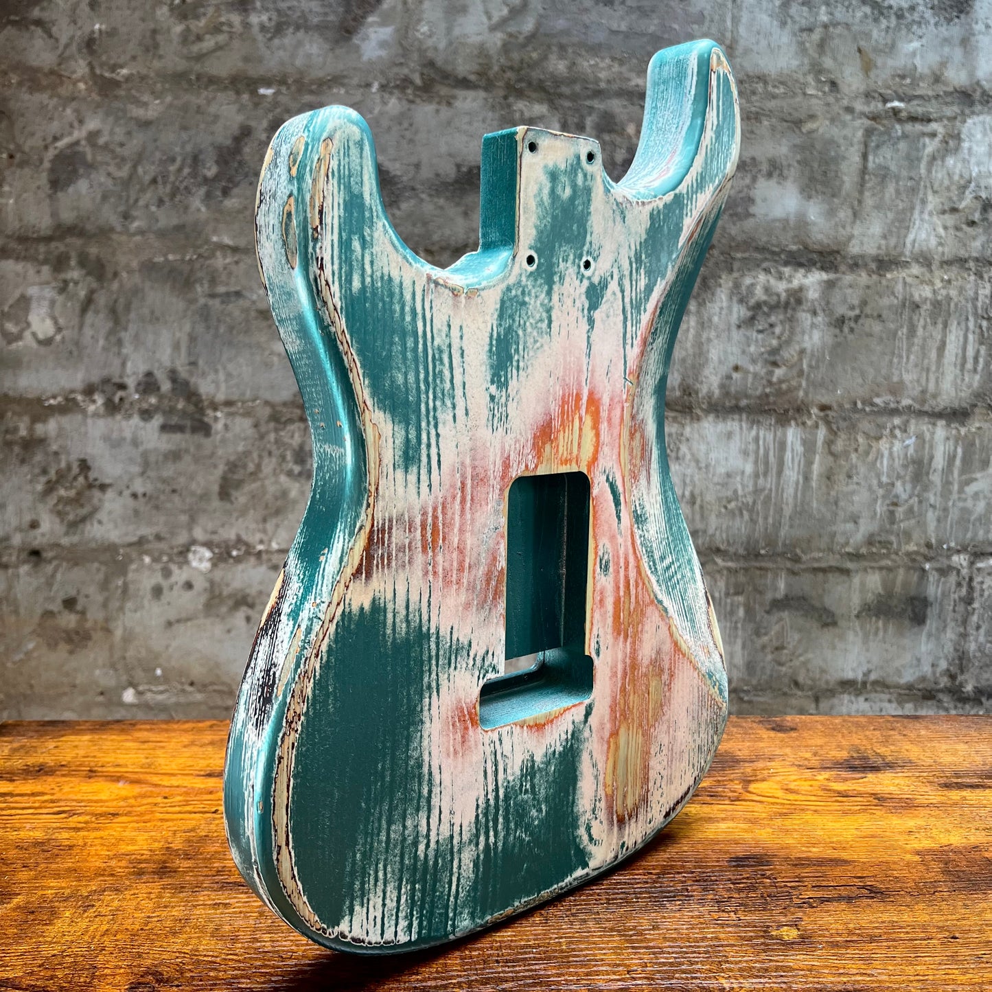 Distressed turquoise and rust-colored guitar body on a wooden surface with a concrete wall background