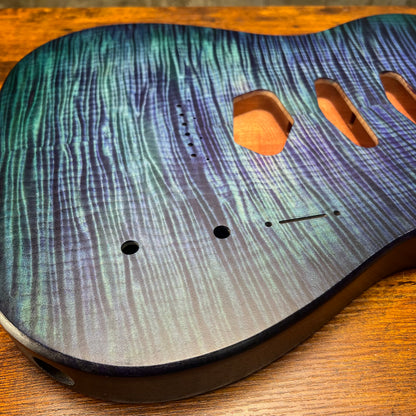 Blue flamed maple Telecaster-style guitar body front close-up with control holes and hardware
