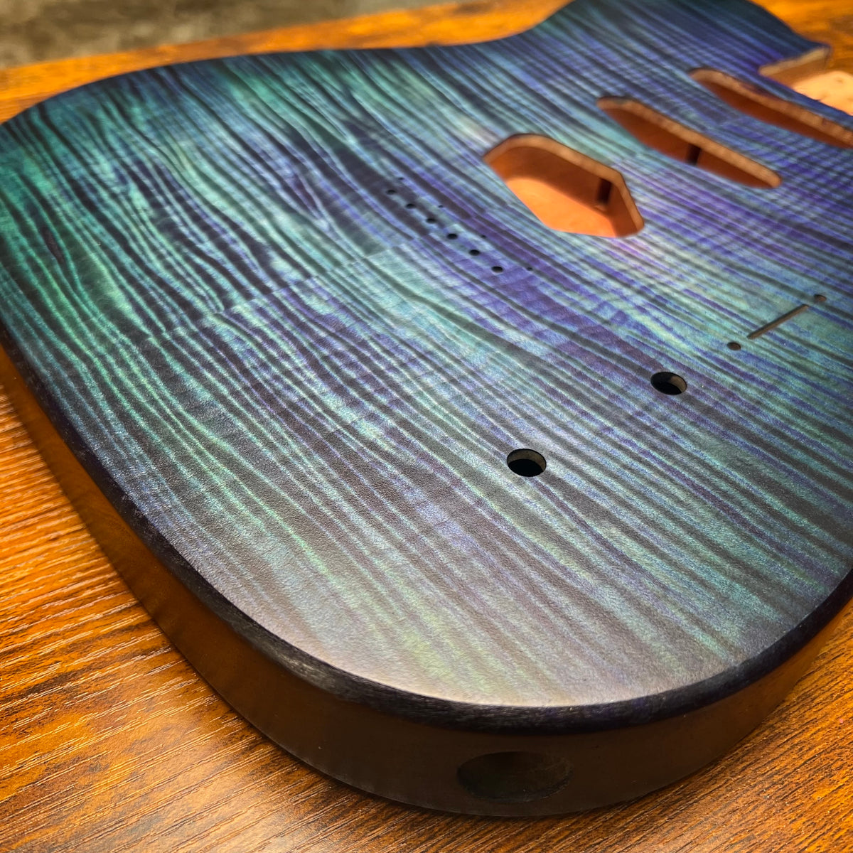Blue flamed maple guitar body front close-up with bridge holes and control route