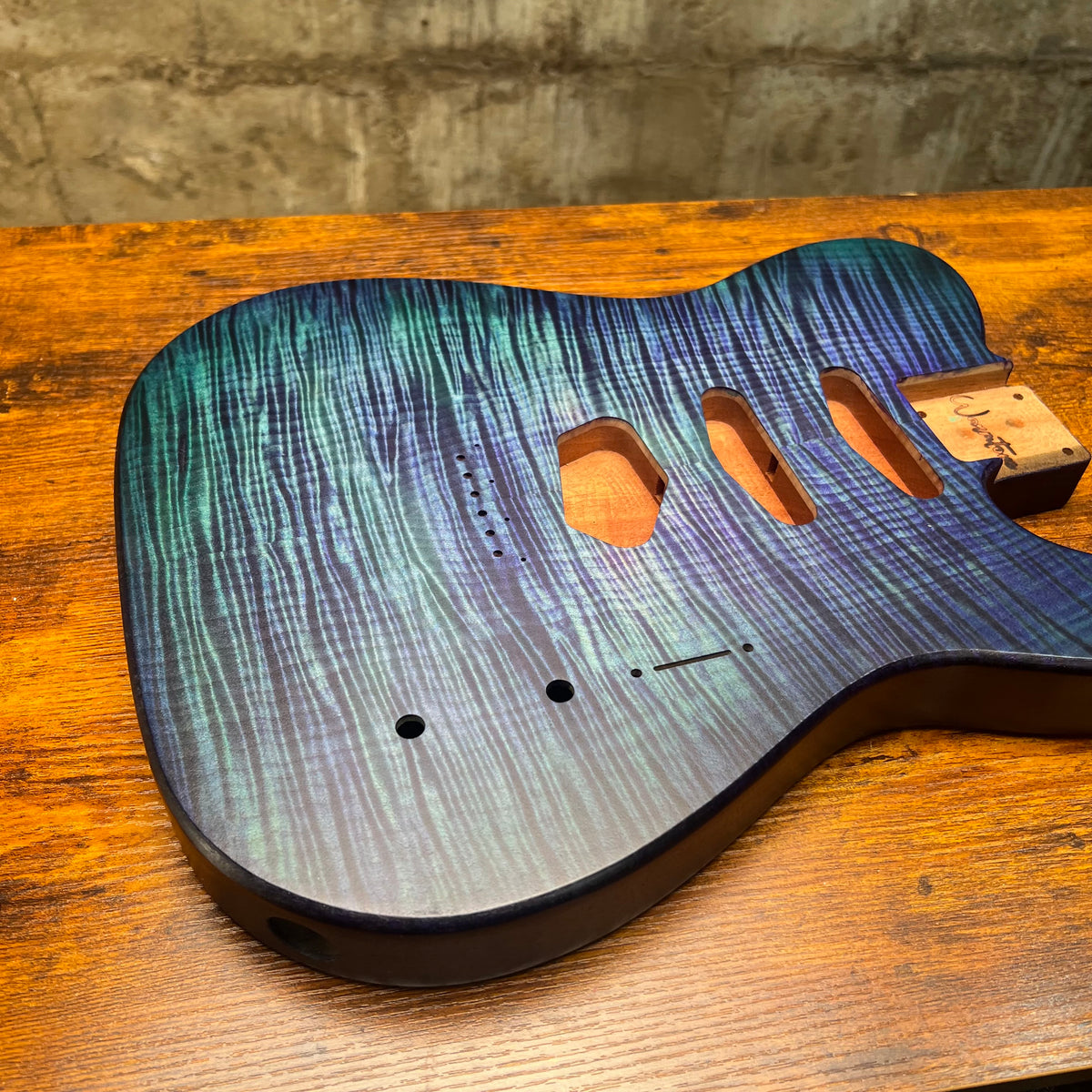 Blue flamed maple Telecaster-style guitar body front with pickup routes and neck plate